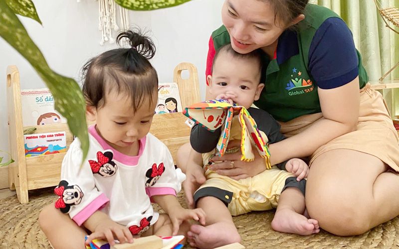 Cô và hai bé chơi với đồ chơi trên sàn lớp